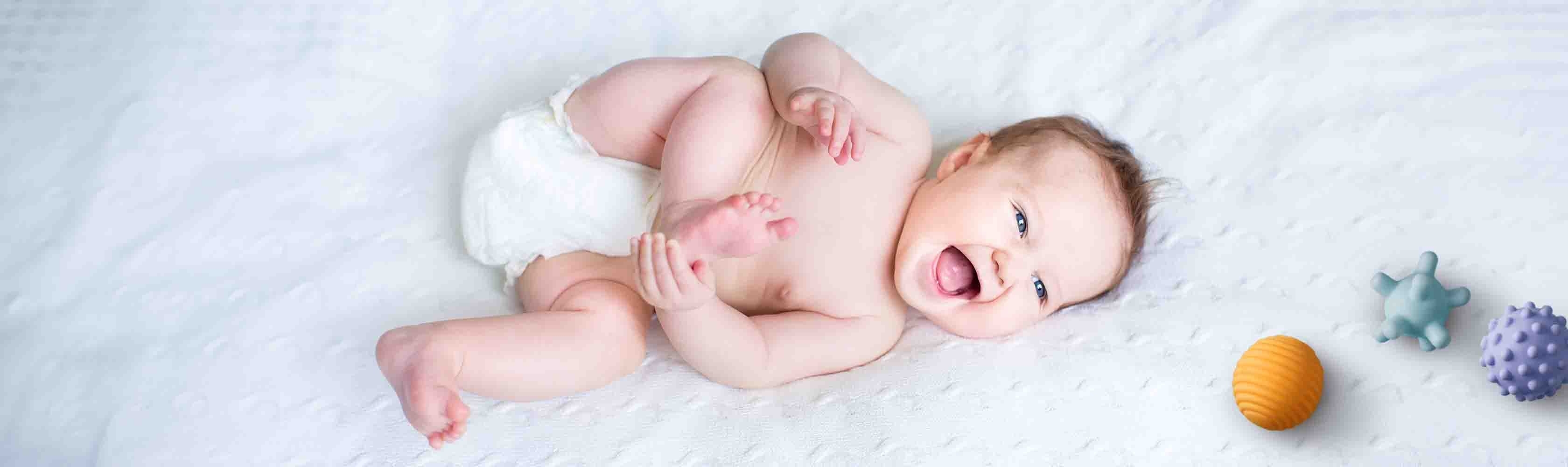 Concorso pannolini - Un bambino in un pannolino è sdraiato sulla schiena accanto ai giocattoli e ride