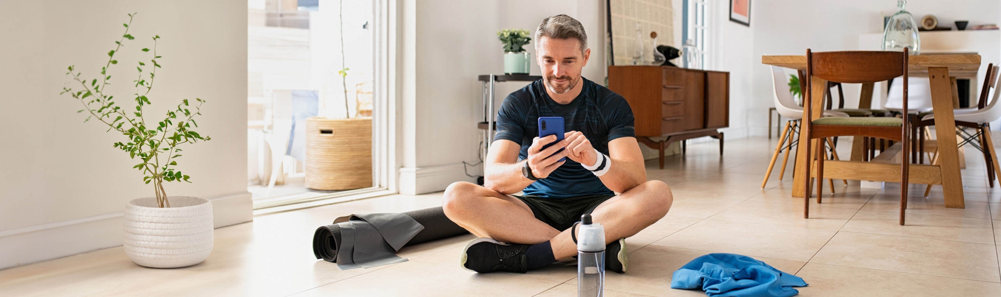Sportlicher Mann benutzt eine Fitness App auf dem Boden sitzend.