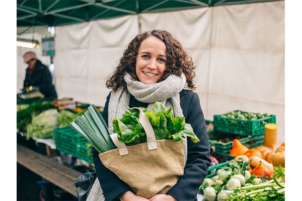 Coline Thomas, Leiterin Übersetzungsdienst bei der CONCORDIA, zeigt sich auf dem Markt mit einer Tasche vollem frischen Obst und Gemüse. Sie übernimmt Verantwortung für ihre Gesundheit.