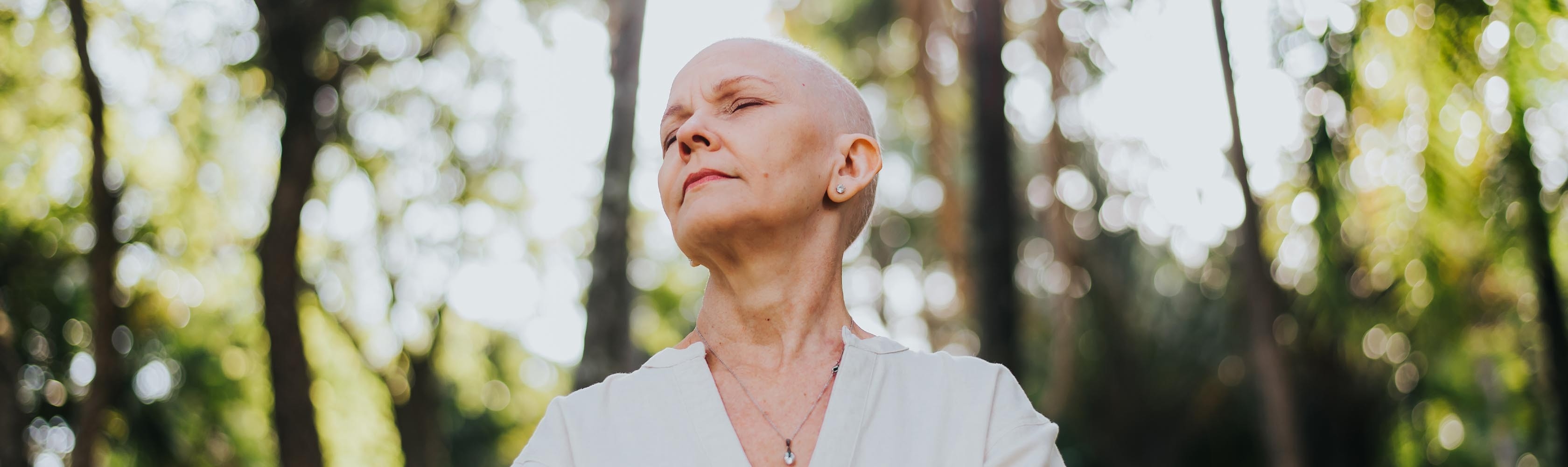 Krebserkrankte Frau steht im Wald bei Sonnenlicht.
