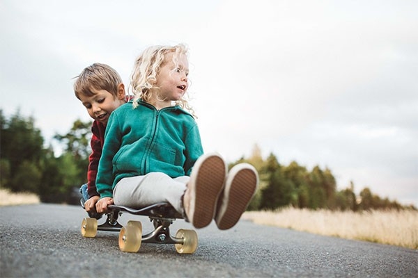 Freundschaft definiert sich bei Kindern über Gemeinsamkeiten: Ein kleines Mädchen und ein kleiner Junge spielen gemeinsam auf einem Skateboard.
