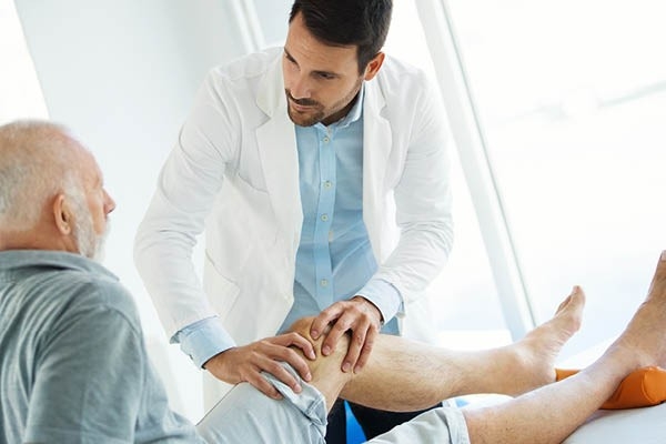 Ein Arzt untersucht das linke Knie eines Patienten.