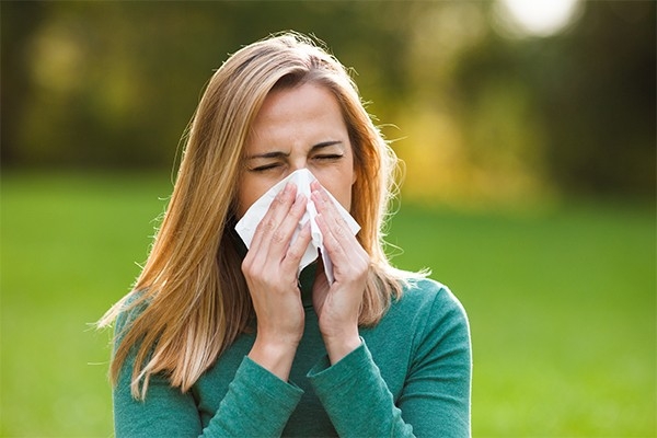 Eine Frau niest in ein Taschentuch. Sie ist allergisch gegen Pollen. Pollenallergien können sogenannte Kreuzallergien verursachen.