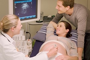 Eine schwangerere Frau und ihr Partner bei der Schwangerschaftsvorsorge. Die Ärztin schaut mittels Ultraschall nach dem Embryo. Die Kosten für Vorsorgeuntersuchungen während der Schwangerschaft übernimmt die Krankenkasse.
