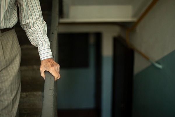 Ein Senior geht vorsichtig die Treppe hinunter und hält sich am Geländer.