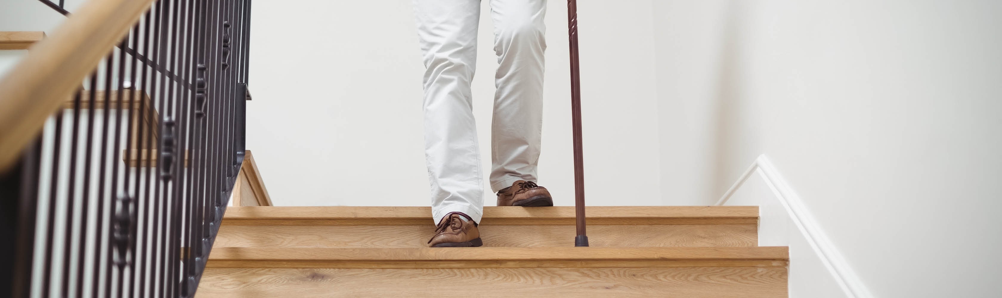 Eine alte Person läuft vorsichtig am Gehtstock die Treppe hinunter
