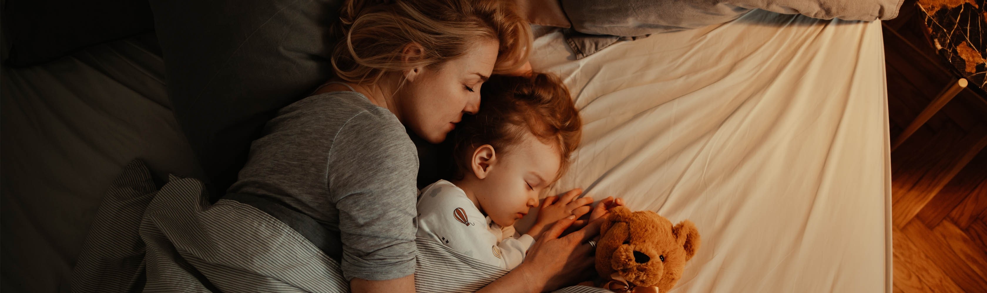 Mutter, Kind und Teddy liegen zusammen im Bett.