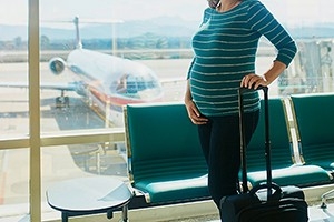 Eine schwangere Frau am Flughafen. Während der Schwangerschaft oder bei konkretem Kinderwunsch sollten Sie sich Ihr Reiseziel gut überlegen.