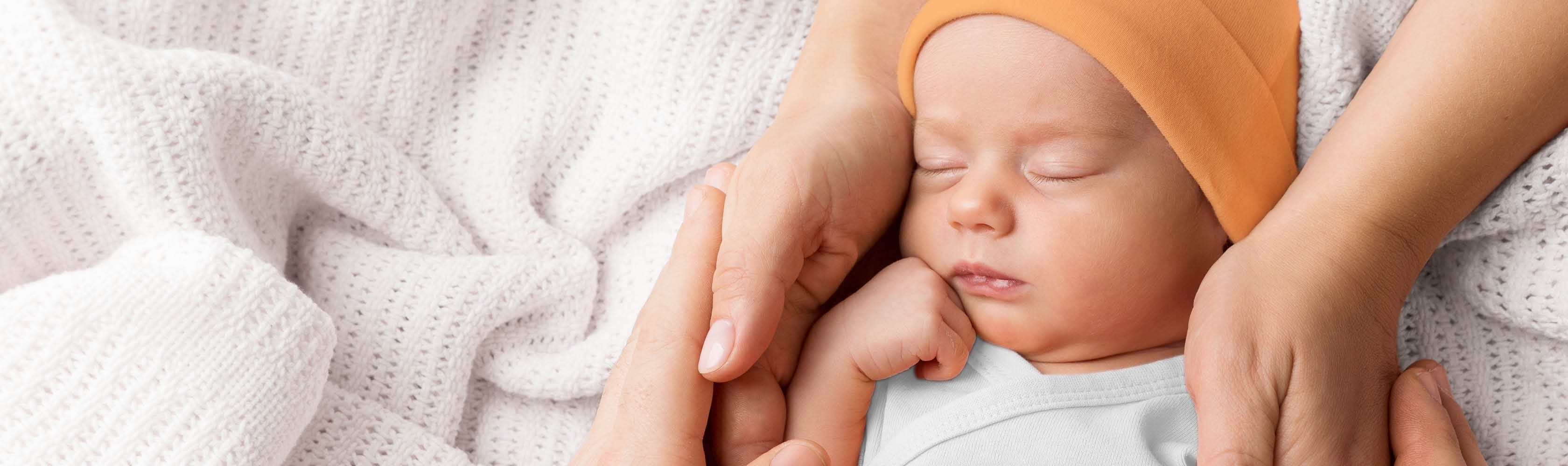 Schlafendes Baby umfasst von den Händen der Eltern