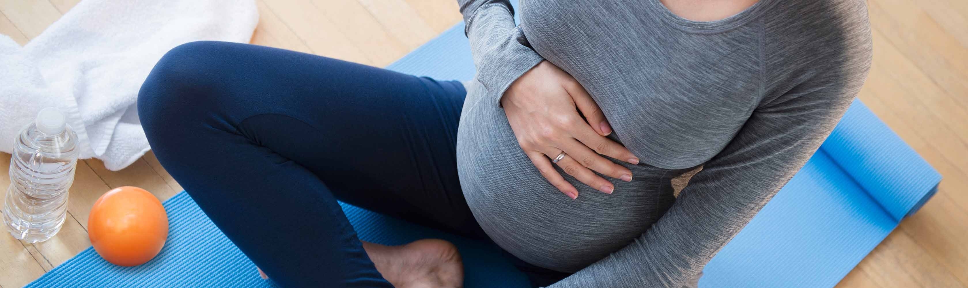 Fit bleiben während der Schwangerschaft - Werdende Mutter auf Yogamatte.