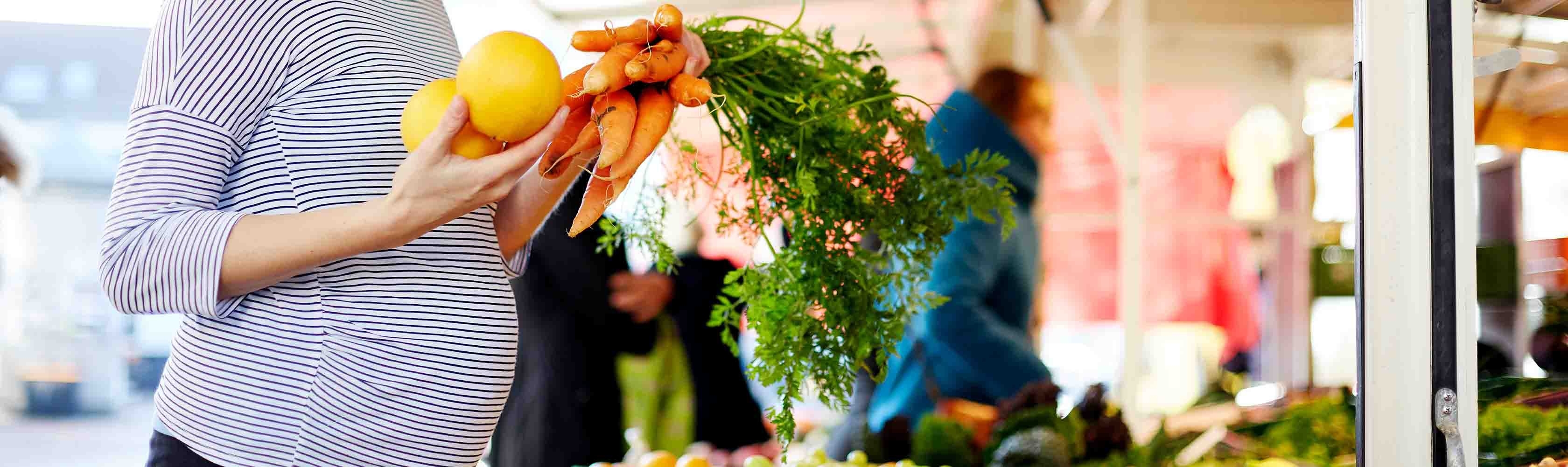 Schwanger werden und Ernährung – Schwangere Frau kauft am Markt frisches Obst und Gemüse.