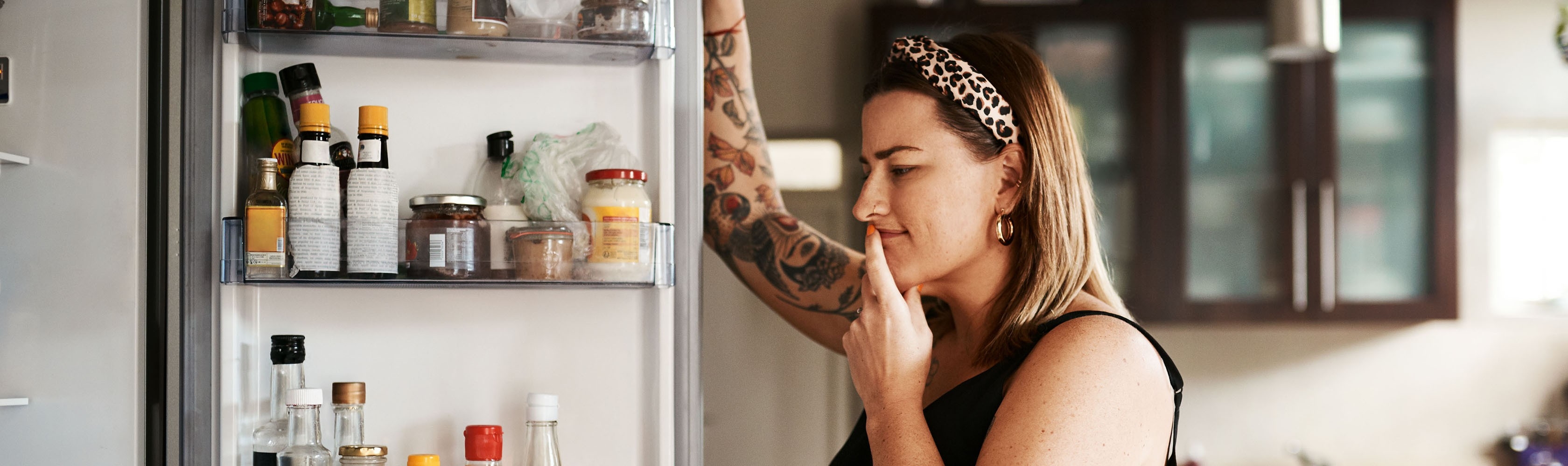 Devant son frigo, une femme se demande quels changements apporter à son alimentation pour manger plus sainement.