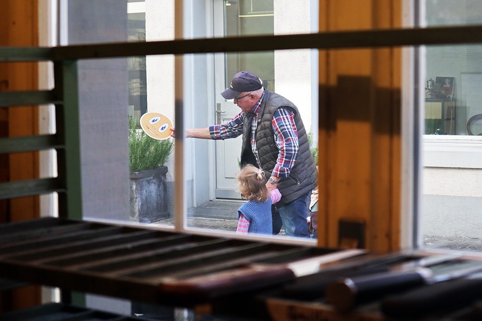 Generationen. Familie. Blick aus dem Fenster der Werkstatt. Ruedi Elsener spielt in der Gasse mit seinen Enkelkinder Frisbee.