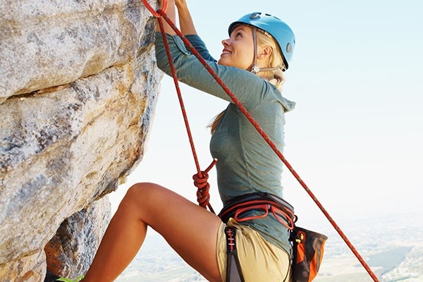 Restez en forme grâce à un entraînement physique diversifié! Bien équipée à l'assaut des sommets: une jeune femme pratique l’escalade, faisant travailler tout son corps. 