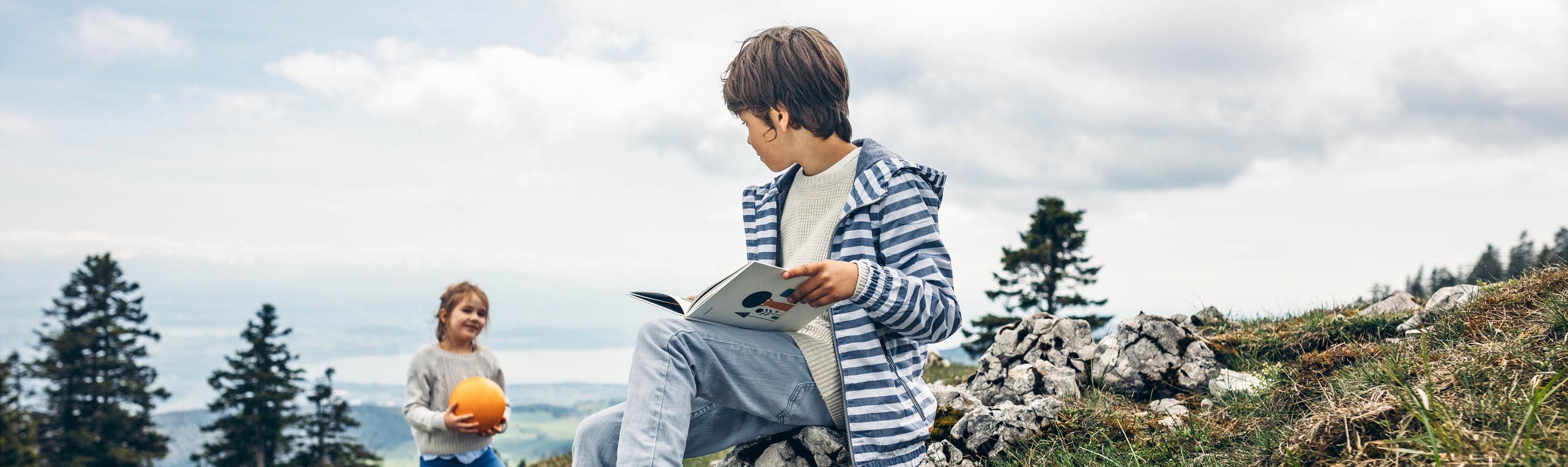 Un garçon est assis sur une pierre et lit un livre.