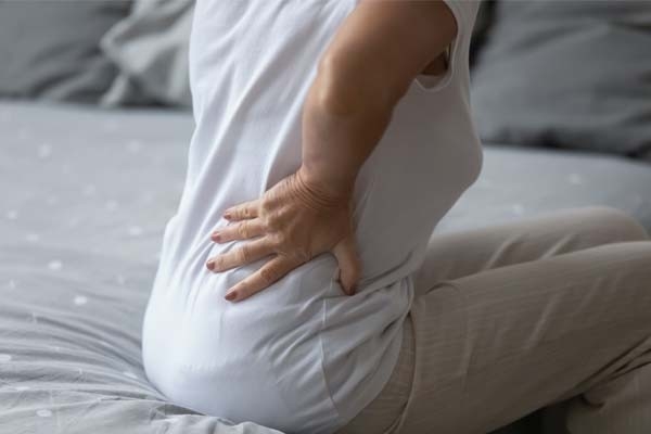 Une femme se tient le dos. Les douleurs dorsales d’origine indéterminée peuvent être un signe d’ostéoporose.