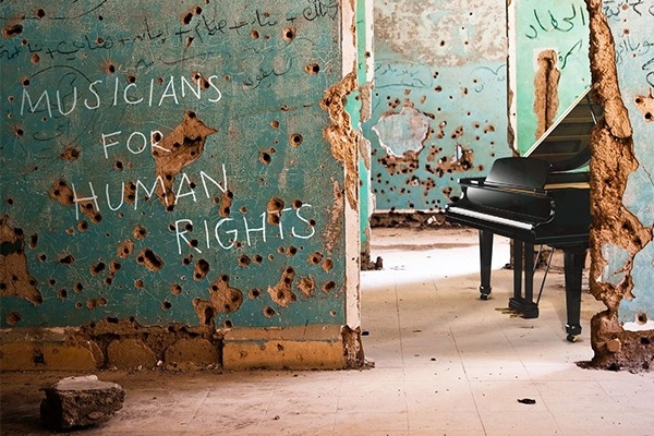 Una vecchia abitazione, con una parete verde crivellata di fori su cui appare la scritta «MUSICIANS FOR HUMAN RIGHTS». Sullo sfondo un pianoforte a coda nero attende i musicisti.