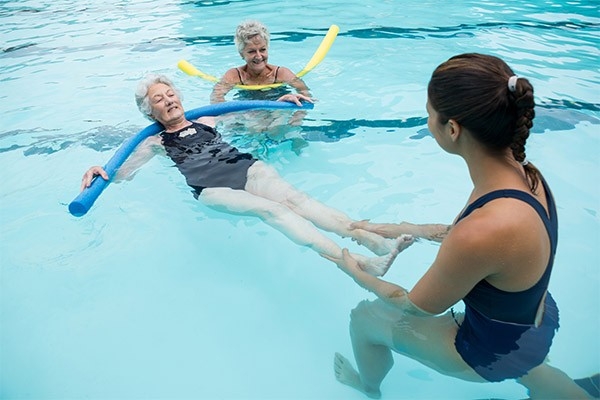 Si può imparare a nuotare anche in età avanzata. Una giovane istruttrice e due signore più avanti negli anni intente a svolgere esercizi di nuoto.
