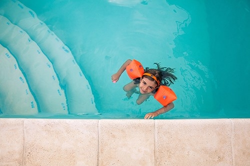 Una bambina nuota in piscina in sicurezza con i braccioli.